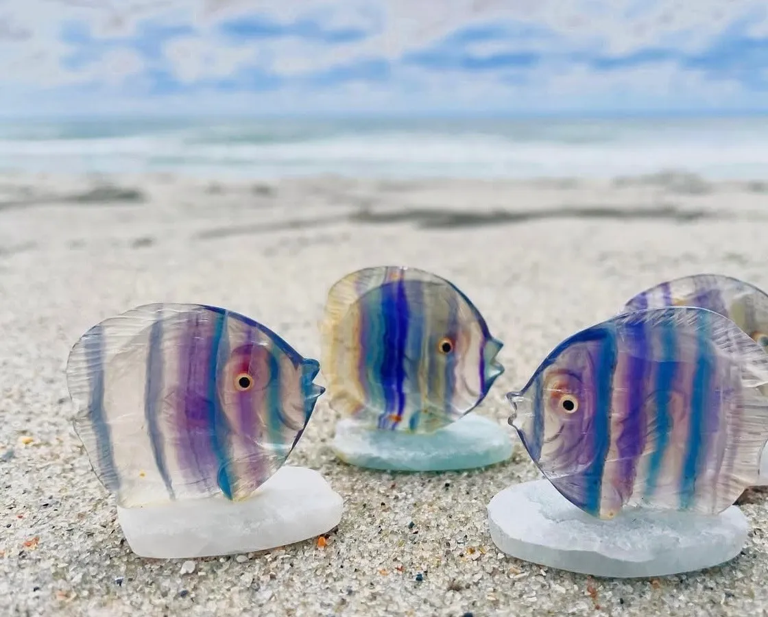 Small colorful glass fish pieces arranged on sand near the ocean.