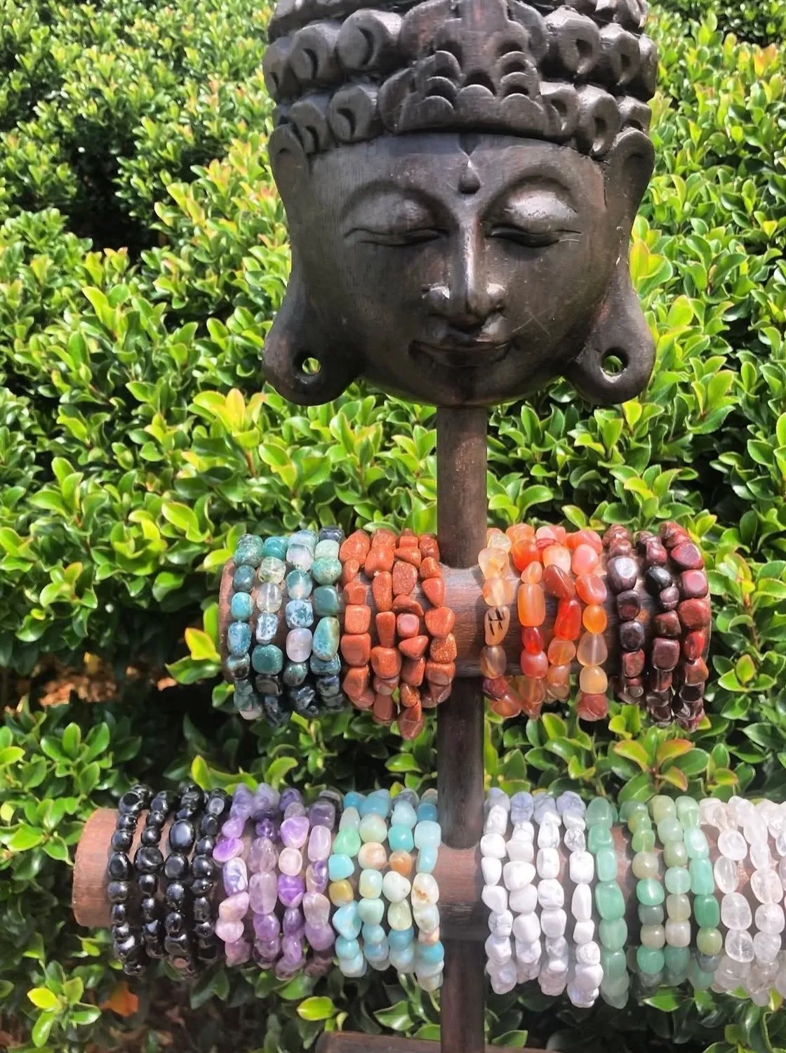 Rows of colorful polished stone bracelets arranged on a dark carved display.